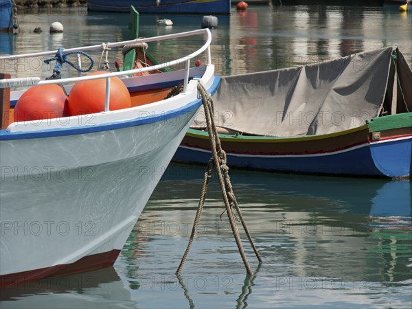 A quiet harbour with anchored boats floating on the reflecting water, marsaxlokk, mediterranean