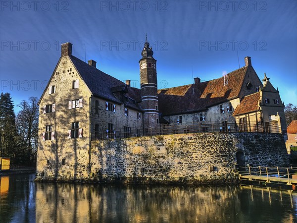 Medieval castle with moat and large tower, which stands out due to a reflection in the water,