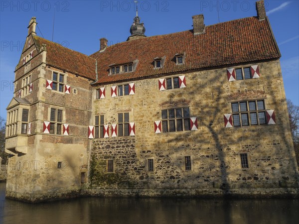 A moated castle with red and white shutters and a red roof, surrounded by water, lüdinghausen,