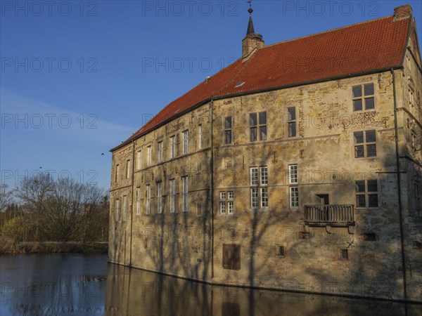 Close-up of a historic stone building with a red tiled roof reflected in the water, lüdinghausen,