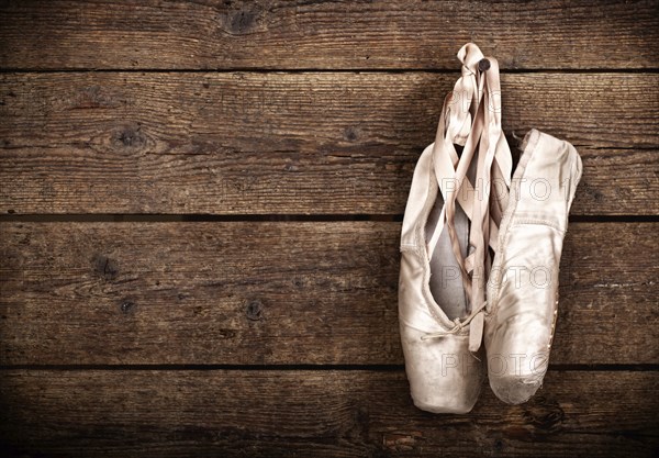 Old used pink ballet shoes hanging on wooden background