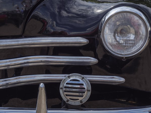 Close-up of a black classic car, showing the front headlight and the chrome grille, winterswijk,