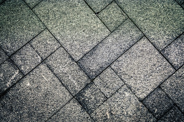 Gray concrete tiles arranged in a geometric pattern creating a rough and textured surface,