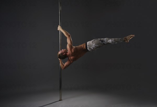 Image of strong gymnast exercising on pylon in studio