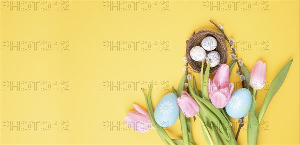 Nest with small eggs and pink tulips on a yellow colored background, easter holiday greeting card,