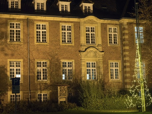 A historic building with illuminated windows at night. The warm light emphasises the details of the