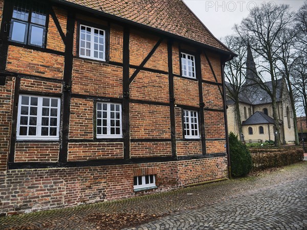 Half-timbered brick house with white windows in an autumnal ambience, church in the background,