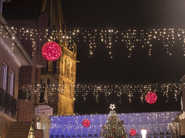 Night shot of an alley decorated for Christmas with fairy lights and a church in the background,