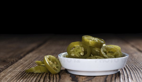 Portion of preserved Jalapenos (close-up shot) on wooden background
