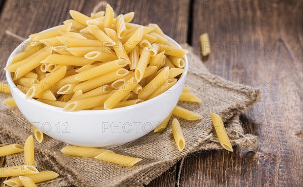 Uncooked Penne (detailed close-up shot) on rustic wooden background
