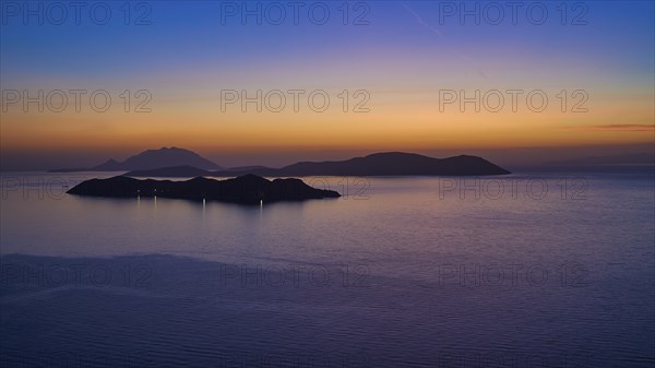 A calm sunset over the sea, the islands in the background surrounded by a gentle colour gradient of