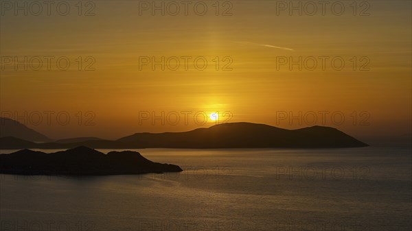 A sunset over the sea, bathing the sky in golden colours and showing tranquil islands in the