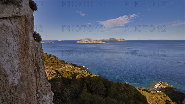 View from a cliff to the open sea and several islands in the distance under a blue sky, Makri