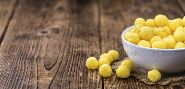 Cheese Balls (fried) as high detailed close-up shot on a vintage wooden table (selective focus)