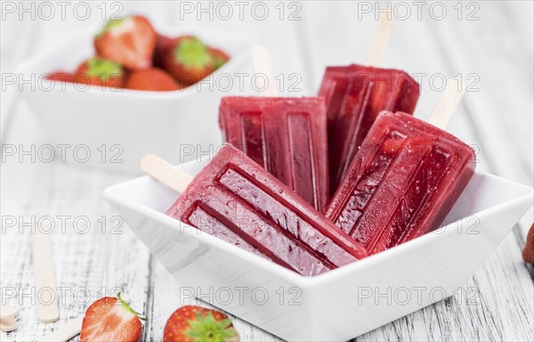 Old wooden table with homemade Strawberry Popsicles (close-up shot, selective focus)