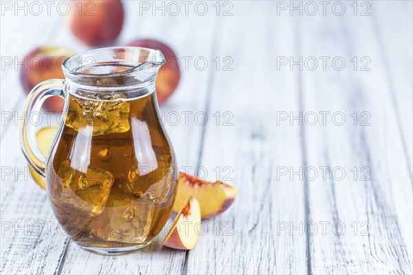 Fresh made peach ice tea (selective focus) on an old wooden table (close-up shot)