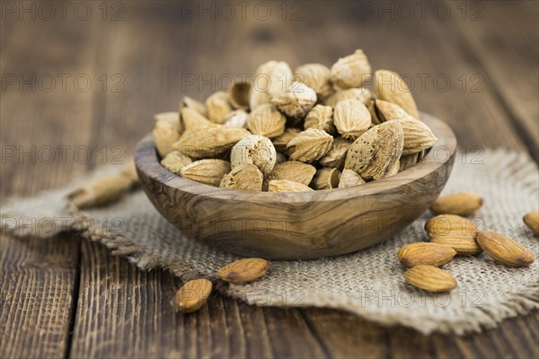 Roasted Almonds (in shell) on an old wooden table (close-up shot, selective focus)
