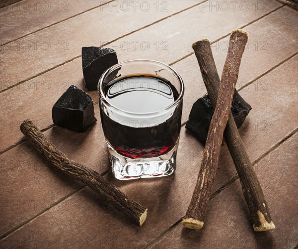 Licorice liqueur with pure blocks and roots on wooden table
