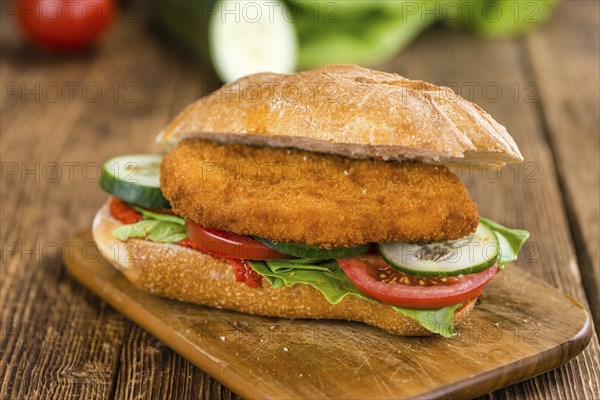 Bun with a Chicken Schnitzel on wooden background (close-up shot, selective focus)