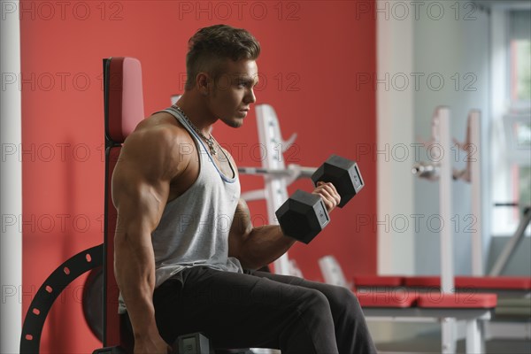 Handsome young man training with dumbbells in gym