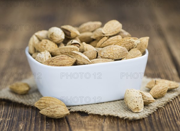Roasted Almonds (in shell) on an old wooden table (close-up shot, selective focus)