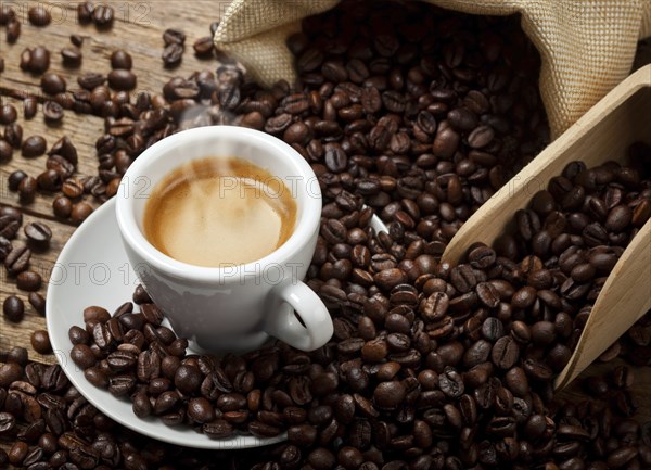 Coffee cup with burlap sack of roasted beans on rustic table, hot coffee