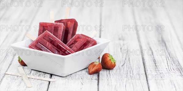 Old wooden table with homemade Strawberry Popsicles (close-up shot, selective focus)