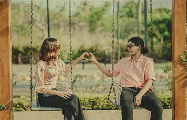 Young couple in love sitting on a swing making a heart shape. Happy couple in love on a park swing