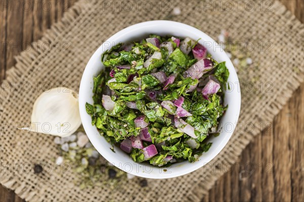 Healthy homemade Chimichurri on a wooden table as detailed close-up shot (selective focus)