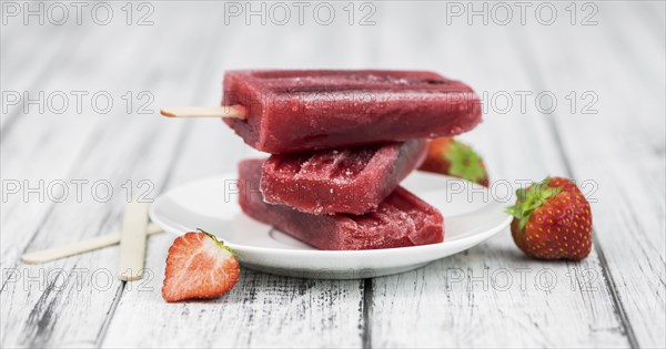 Old wooden table with homemade Strawberry Popsicles (close-up shot, selective focus)
