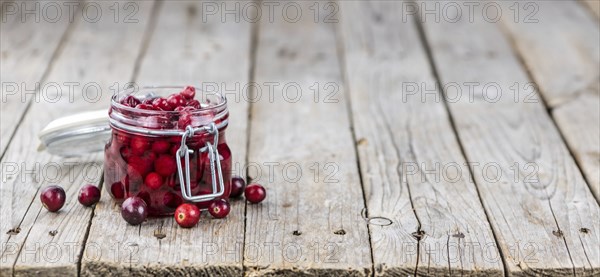 Old wooden table with fresh Preserved Cranberries (close-up shot, selective focus)