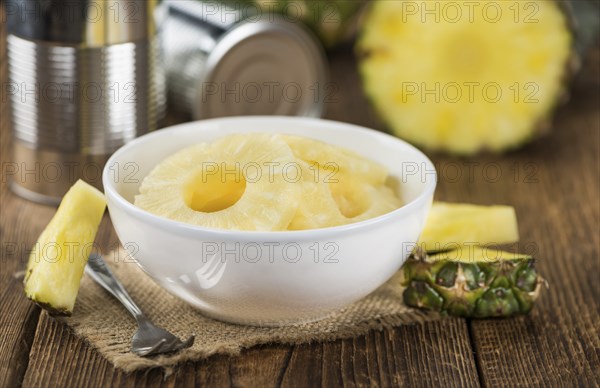 Preserved Pineapple Rings as high detailed close-up shot on a vintage wooden table, selective focus