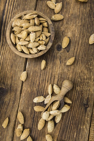 An old wooden table with roasted Almonds (in the shell) as detailed close-up shot (selective focus)