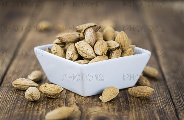 An old wooden table with roasted Almonds (in the shell) as detailed close-up shot (selective focus)