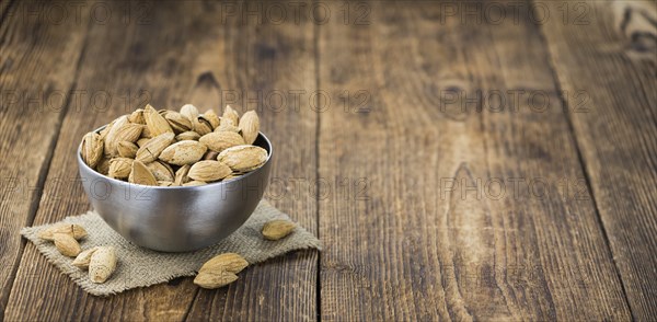 Roasted Almonds (in shell) on an old wooden table (close-up shot, selective focus)