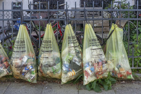Yellow bags for plastic waste, hanging on a garden fence in front of a house entrance, waste