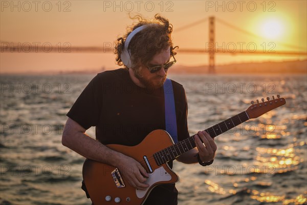 Hipster street musician in black playing electric guitar in street outdoors on sunset