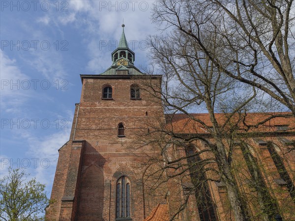 Impressive Gothic-style brick church tower surrounded by trees under a partly cloudy sky, lüneburg,