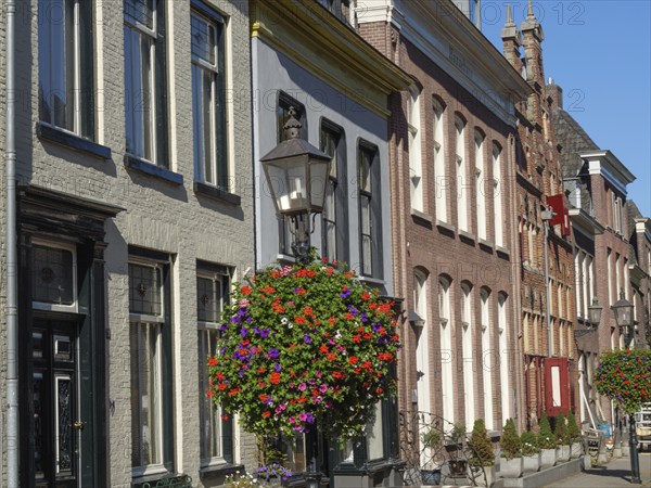 Street scene with terraced houses, large windows and hanging flower baskets under a clear sky,