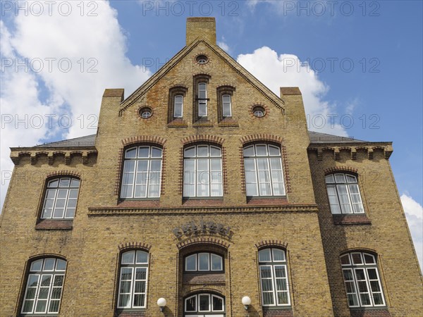 Large, multi-storey brick building with numerous windows and a clear sky, Kappeln,