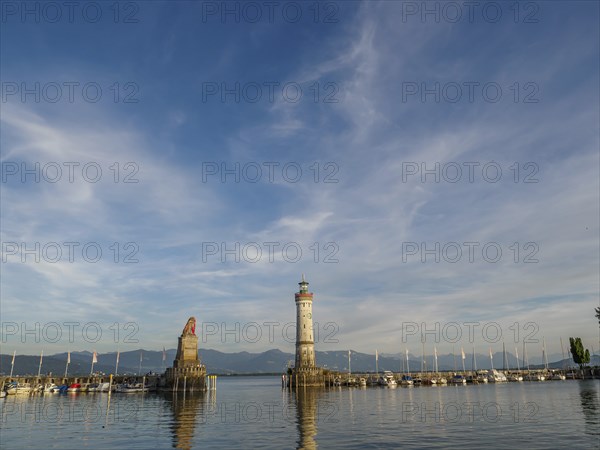 A harbour with a lighthouse and a fisherman's statue, surrounded by boats and mountains in the