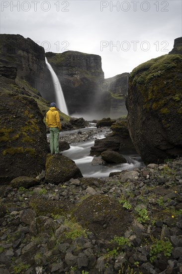 Young man with yellow jacket standing in front of waterfall, Haifoss and Granni waterfall at a