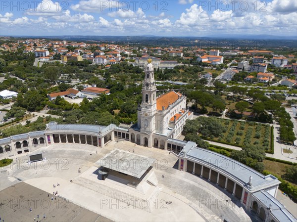 High angle shot of a basilica with a large square surrounded by green trees, sky with clouds,