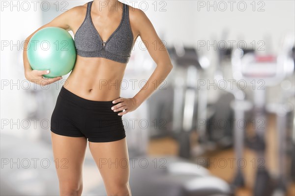Fit woman standing and holding a pilates ball, in a gym