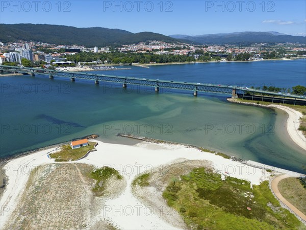 View of a coastal town with a bridge over a river flowing into the ocean, surrounded by hills and