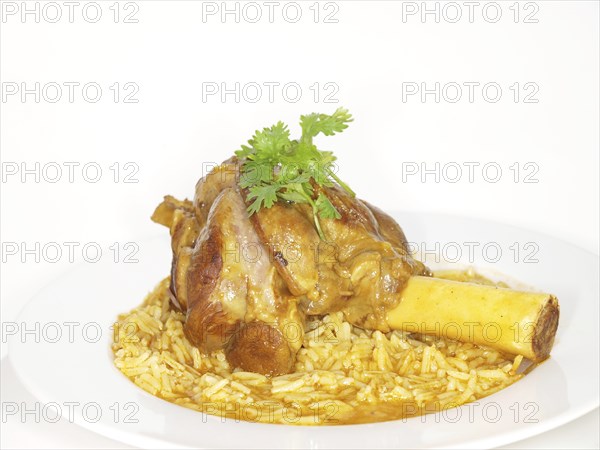 Lamb shank in juicy yellow rice, on white plate towards white