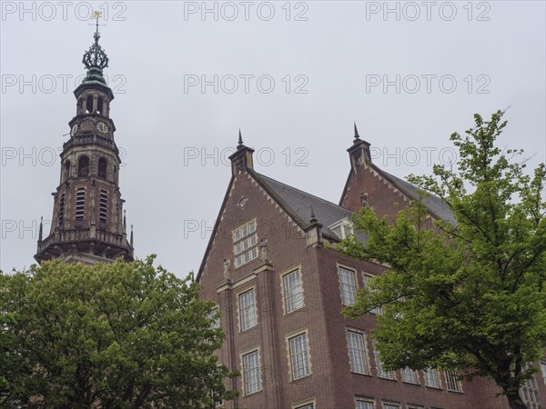 Historic building with imposing church tower and trees in the foreground under a grey sky, Leiden,