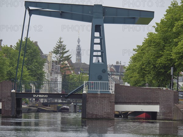 A bascule bridge over a canal with a church tower in the background and tree-lined streets, Leiden,