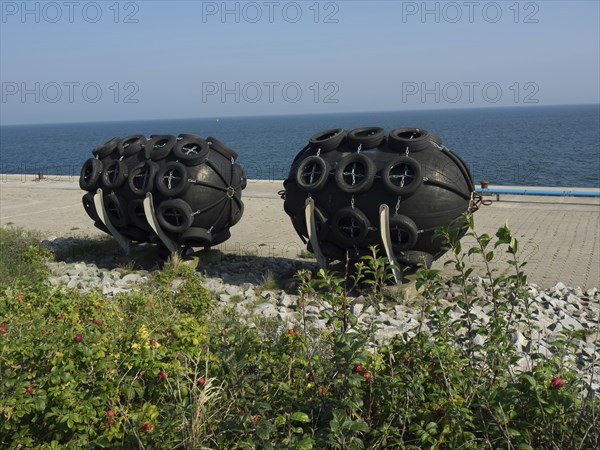 Black round fenders on the shore next to the blue sea under the clear sky, helgoland, germany
