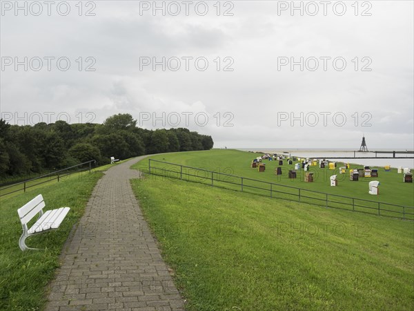 A paved path and a bench lead to a meadow with colourful beach chairs, cuxhaven, germany